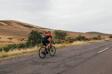 Fototapeta na wymiar Back view of sportswoman cycling road bike on empty countryside road