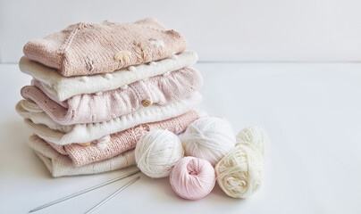 Stack of knitted clothes and balls of yarn, knitting needles, accessories for knitting. Baby clothes. Needlework, hobby, knitting, handwork.