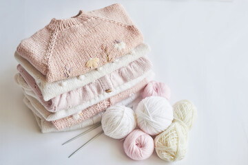 Stack of knitted clothes and balls of yarn, knitting needles, accessories for knitting. Baby clothes. Needlework, hobby, knitting, handwork.