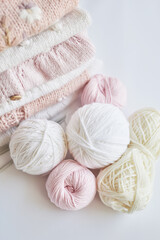 Stack of knitted clothes and balls of yarn, knitting needles, accessories for knitting. Baby clothes. Needlework, hobby, knitting, handwork.