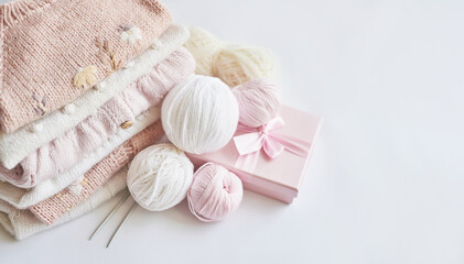 Stack of knitted clothes and balls of yarn, knitting needles, accessories for knitting. Baby clothes. Needlework, hobby, knitting, handwork.