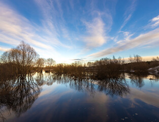 Epic spring landscape by the river. The flood of the river in early spring. A colorful sunset is reflected in the water. March evening landscape.