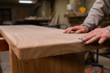 Closeup of person sanding wooden table using sandpaper in workshop