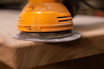 Closeup of carpenter sanding wood table with orbital sander in a workshop © Collab Media