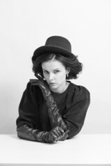 curly woman in a hat and gloves sits at a white table, black and white photo