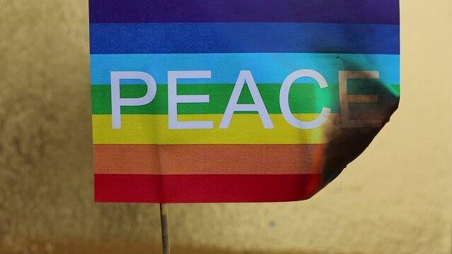 Multicolored Flag with the text PEACE burning with the golden background symbolizing war and destruction