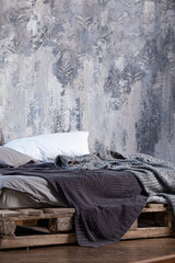 Pillows and mattress on a makeshift pallet bed, covered with gray blankets.
