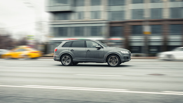 side view rolling shot in gray color crossover car in motion. Audi Q7 driving along the street in city with blurred background