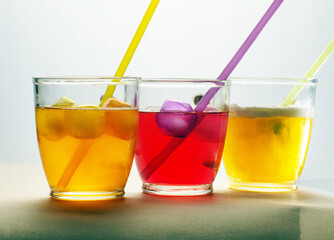 Three glass cups with yellow and red drinks with straws and ice cubes