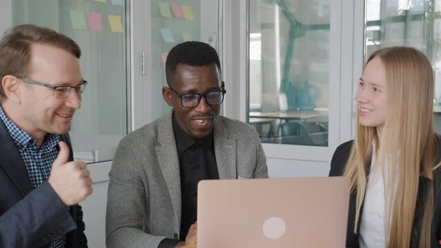 Multinational ethnic diverse business team celebrate success, got positive successful results. Colleagues have meeting in office, looking in laptop screen, received email, profitable deal, good news