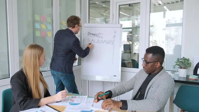 Business meeting with presentation of business plan, new project or marketing strategy. Man writing on flipchart and communicating with colleague partner. Office workers coworkers conference