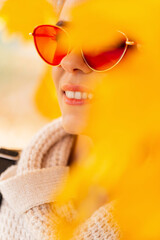 Autumn bright colored portrait of a beautiful happy young woman with a smile and red sunglasses in the yellow autumn leaves in the park