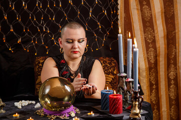 A bald woman fortune-teller tells fortune-telling on white pebbles by candlelight in the salon.