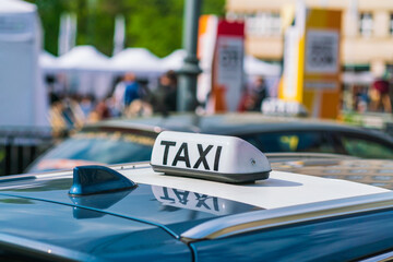The inscription TAXI is reflected on the roof of the car on a sunny day against a blurred background of another taxi car, city street and passers-by