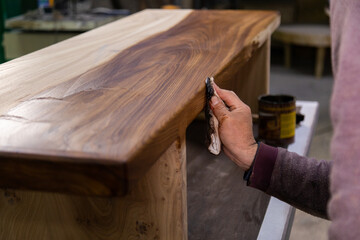 Closeup of carpenter coating a wooden table with protective flaxseed oil