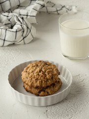 Oatmeal banana cookies with  chocolate drops on the white ceramic plate, glass of milk, milk jug. White background. High key