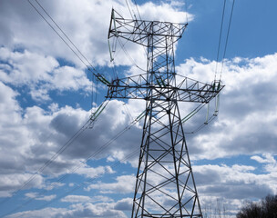 Tower of a high-voltage power line against the of blue sky and clouds