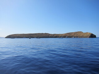 Side view of Molokini, a crescent-shaped volcanic crater and small islet. Destination for scuba diving, snuba, and snorkeling. Deep blue sea, blue sky and tourist boats. Maui, Hawaii.