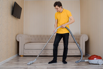 man in a yellow t-shirt is vacuuming the wood flooring  using a vacuum cleaner.   .