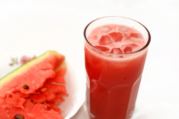 A fresh watermelon smoothie juice drink with ice cubes and a plate full of Slices of watermelon...