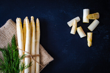 Bunch of raw white asparagus and dill on black background
