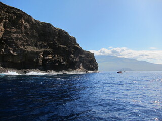 Big rocky island, deep blue sea, blue sky and tourist boats. View of Molokini islet at Maui, Hawaii. Small boat heading towards the island.
