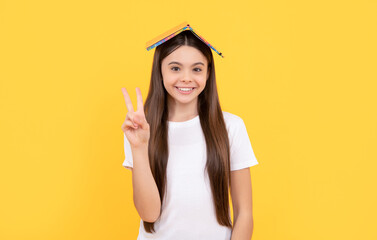 happy teen girl hold book showing peace on yellow background, school