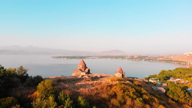 Aerial ascending view Armenian Monastery of Sevanavank in sunny day with Lake Sevan background, Sevan Peninsula, Armenia