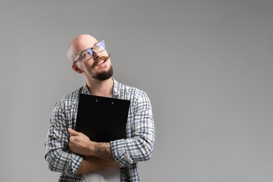 Smiling Balded Bearded Man Hold Clipboard Looking Away From Camera Isolated On A Grey Background