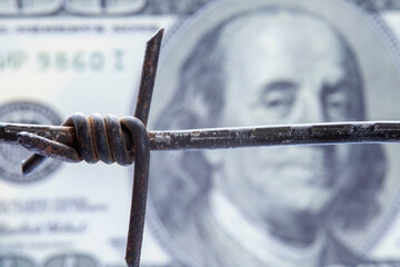 Economic warfare, sanctions and embargo busting concept. US Dollar money wrapped in barbed wire. Selective focus on barbed wire. Horizontal image. - obrazy, fototapety, plakaty