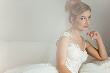 Fototapeta na wymiar Beautiful bride sitting on a white sofa and looking at the camera