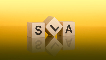 Three wooden cubes with the letters SLA on the bright yellow surface. the inscription on the cubes is reflected from the gray surface of the table. SLA - short for Service Level Agreement
