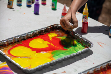 Colorful Oil Dipped Painting in a Tray of Water with a Hand Designing a Pattern in the Paint
