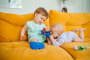 Fototapeta na wymiar two babies playing on a yellow sofa