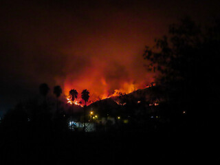 Naklejka na ściany i meble A Mountain Wildfire in San Bernardino, California, with the night sky Shining Orange with Smoke from the Fire