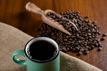 Green cup of coffee with coffee beans on wooden background	