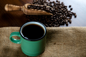 Green cup of coffee with coffee beans on wooden background	