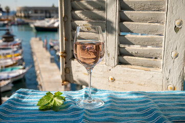 Rose wine in glass served on outdoor terrace with view on old fisherman's harbour with colourful...