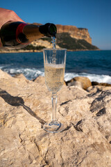 Pouring of French champagne sparkling wine in glass and view on beach and mountains in Cassis, Provence, France