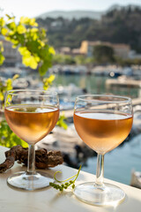 Cold rose wine in glasses served on outdoor terrace in sunlights with view on old fisherman's harbour with colourful boats in Cassis, Provence, France
