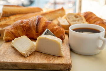 Fototapeta na wymiar French breakfast with fresh baked croissants, baquett bread, crottin goat cheese, black coffee and view on fisherman's boats in harbour of Cassis, Provence, France