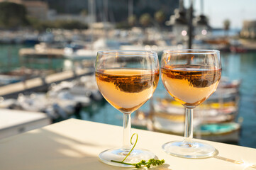 Summer party with cold rose wine in glass served on outdoor terrace in sunlights with view on old fisherman's harbour with colourful boats in Cassis, Provence, France