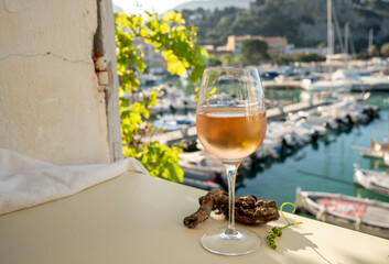 Cold rose wine in glass served on outdoor terrace in sunlights with view on old fisherman's harbour with colourful boats in Cassis, Provence, France