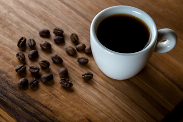 White cup of coffee with coffee beans on wooden background