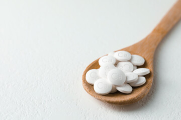 Fototapeta na wymiar Calcium supplement pills in wooden spoon on white table, closeup. Space for text
