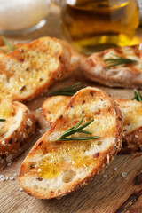Tasty bruschettas with oil and rosemary on wooden board, closeup