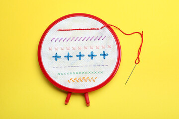 Fabric with colorful stitches in embroidery hoop and needle on yellow background, top view - obrazy, fototapety, plakaty