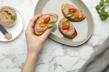 Woman taking slice of bread with delicious pate at white marble table, top view
