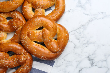 Delicious pretzels with sesame seeds on white marble table, flat lay. Space for text