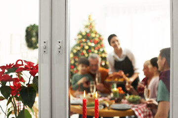 Happy family enjoying festive dinner at home, view from outside. Christmas celebration